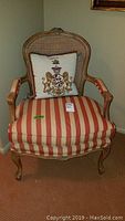 Front view showing chair with striped seat cushion and heraldic needlepoint pillow, carved wood frame, and caned backrest.