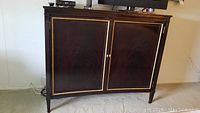 Front view of mahogany cabinet with two gilt-trimmed doors and brass knobs, eggplant finish