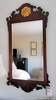 Full front view of one mahogany wall mirror showing wood frame with gold leaf applique at top and rectangular mirror glass.
