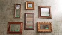 Six small framed mirrors arranged on a textured wall, showing various gold and bronze ornate frames in rectangular and square shapes.