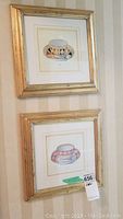 Two framed prints of decorative tea cups, hung vertically on a striped wallpapered wall.