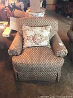 Front view of custom club chair with floral pillow and dressmaker skirt, showing patterned upholstery and rolled arms.