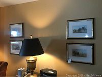 Wall showing two framed golf art prints positioned above a lamp and furniture, illustrating the overall condition and framing style.