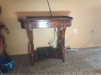 View of the console table showing its shape, drawer, and lower shelf with an electronic device on it.