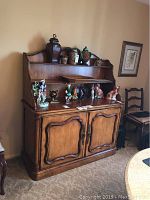 Front view of wood server with nailhead trim, decorative molding, two open shelves with various decorative items displayed.