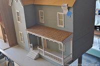 Front approach of the doll house showing the porch steps, railing, and three windows on the main face.