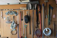 Full view of garden tools hung on pegboard including shovels, hoes, rakes, tennis rackets, and hand tools