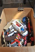Cardboard box filled with assorted loose Lego pieces and partially built Lego elements.