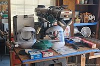 Wide view of radial arm saw on workbench with helmets, gauges, and accessories displayed.