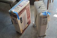 Two electric radiator heaters with one original box on concrete floor.