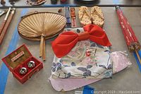 Top-down view of kimono set laid out with five fans, red bow belt, parasol, slippers, and Chinese iron exercise balls box