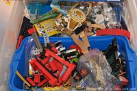 Assorted loose LEGO pieces including red, black, beige, and other colors in plastic bins and bags.