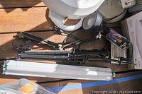 Overview of lot showing white LED flushmount light fixtures, two black adjustable desk lamps, and assorted lighting parts on wooden surface.