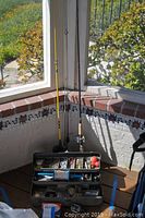 Three fishing poles standing upright with attached reels and a black tackle box with compartments holding various fishing gear including lines, floats, and lures.