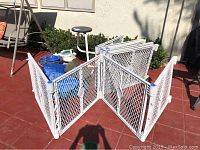 White plastic expandable baby gates assembled outdoors on red tile ground; multiple panels joined in zig-zag shape