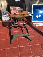 Full view of Black & Decker WorkMate 200 portable workbench on red tile floor with various items in background including a bag of potting soil and a blue screen.