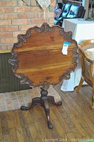 Front view of hand carved wood table with scalloped edges and carved pedestal base.