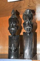 Front view of two ebony wood statues with detailed facial features and textured torsos.