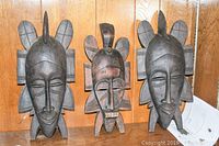 Photo of the three wooden carved masks grouped together showing front views and relative sizes.