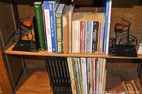 Full view of two wooden shelves holding books and magazines with metal bicycle bookends on the top shelf