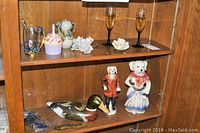 Two wooden shelves holding various decorative objects including dog figurines, wooden duck decoy, glassware and porcelain pieces