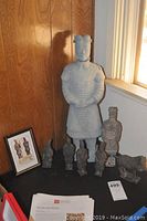 Full view of all replicas on display including a framed photo, one large soldier and several smaller soldier replicas arranged on a black surface by a wood-paneled wall.