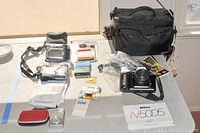 Overview of the lot on table with Nikon N5005 AF camera, Olympus Stylus camera, Olympus Camedia D360L digital camera, JVC GRD270 video camera, cases, cleaning kit, tapes, batteries, and instruction manuals.