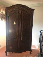 Full view of vintage wooden Heritage armoire with carved floral and scroll designs, two doors and brass handles.