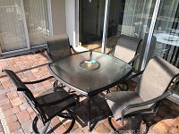 Full view of lanai patio set showing square glass table with center lazy Susan and 4 swivel chairs with mesh fabric seats and backs on brick patio.