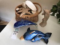 Overview photo showing stone dolphin sculpture, blue glass dolphin, ceramic dolphin with smaller dolphin, and basket with shells and starfish.