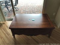 Rectangular wooden coffee table with 4 drawer fronts, two drawers open, shown from top-down front view on wood flooring near patio door.