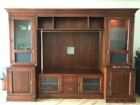 Front view of entire wood wall unit showing middle TV space, upper open shelves, drawers, glass-front cabinets on bottom, and side towers with closed doors