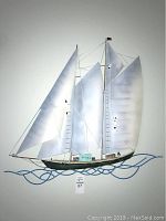 Front view of metal ship wall art showing three large white sails, masts, rigging, and blue wave design below.