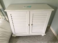 Front view of the white cottage cabinet with two shutter doors and round knob handles.