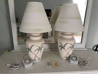 Two palm tree ceramic table lamps with beige shades on a dresser, with timer switches visible on the cords.