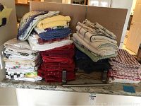 Photo of kitchen towels stacked on a marble countertop and held with a metal holder, showing various folds and colors.