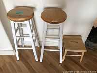 Two swivel bar stools with wood seats and white legs next to small wooden step stool