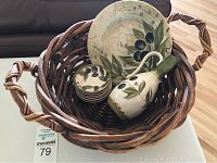 Woven dark brown basket containing ceramic olive-themed dishes including large plate, six small bowls, and oil dispenser