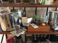 Full view of metal ice bucket, wooden case with bottle opener, plastic 'Happy Hour' mug, and some accessories on a wooden shelving unit.