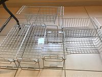 Top-down view of five metal wire kitchen racks arranged on floor, showing basket and shelf styles with handles.