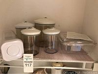 Overview of six FoodSaver canisters of varying sizes with white lids and one rectangular vacuum sealer container with lid