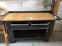 Front view of the Craftsman workbench showing wooden top, black metal frame, and two metal drawers.