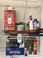 Photo showing the Roundup garden sprayer, garden trimmers, pruning shears, pest control sprays, Rose & Flower Care bottle, and box of Kirkland trash bags on shelves.