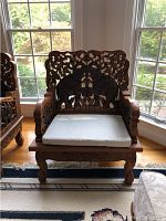 Front view of carved teak chair with cushion, showing elephant carvings and detailed craftsmanship.