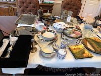 Overview of silverplate serving trays, bowls, dishes, blue and white dishware, and decorative plates arranged on a table.