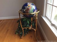 Wide shot showing globe on brass stand with faux plant in wicker stand beside window