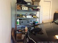 Full view of metal shelving unit in garage next to car, contents on shelves and wear from storage visible