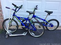 Photo showing two kids bikes and a scooter side by side on driveway in front of garage door: 16-inch Murray Hammerhead, 14-inch Kent Action Zone, and Razor scooter with purple grips.
