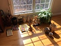 Wide view of lot items arranged under window with natural light showing lamp shades, brass stand, waste cans, carved stone grapes, decorative figures, picture frames, and parasols.
