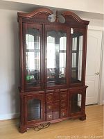 Full view of a wooden china cabinet standing on hardwood floor, top half has glass doors and shelves, bottom half has drawers and cabinets with glass inserts.